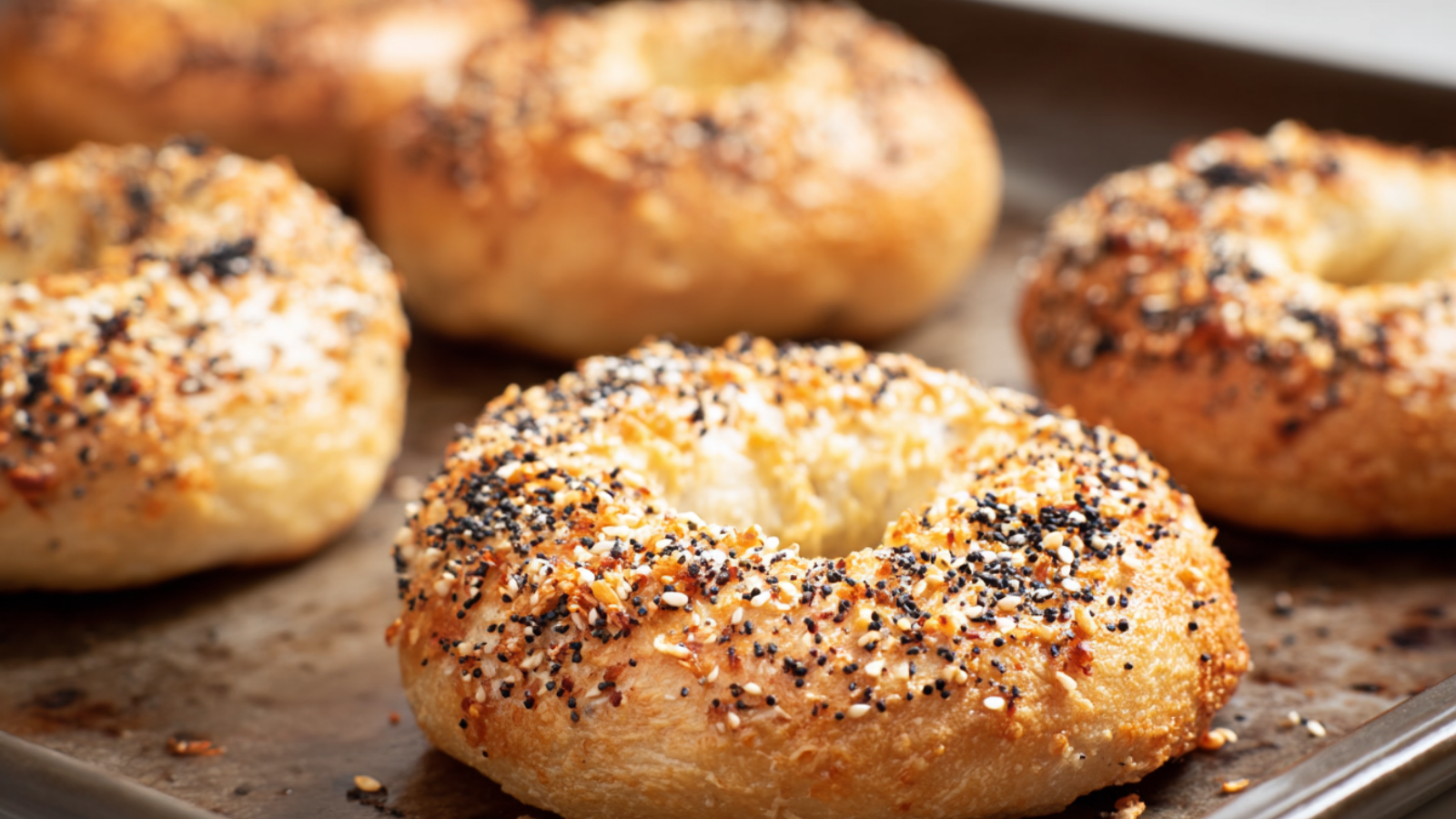 Close-up of golden-brown low carb bagels topped with everything seasoning, fresh out of the oven on a baking tray
