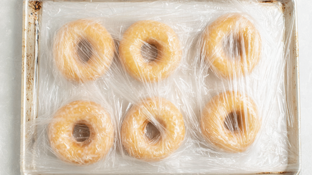 Tray of shaped bagels wrapped in plastic, resting in the fridge for overnight proofing