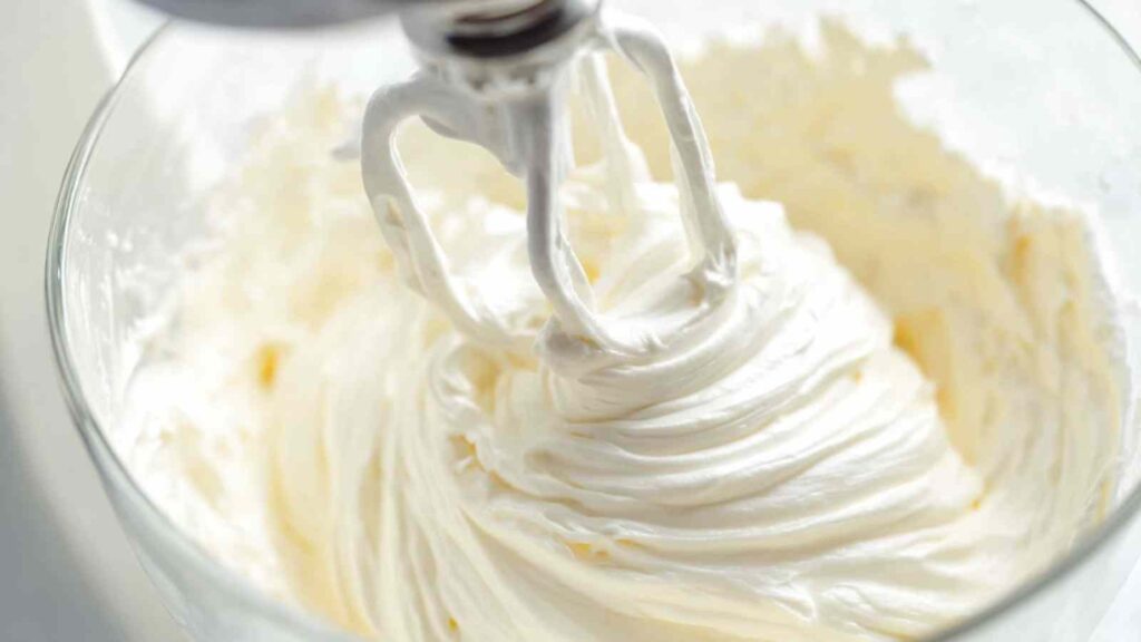 Close-up of cream cheese being whipped in a stand mixer, showing airy texture forming