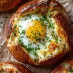 Close-up of single cheesy egg bagel with crispy crust and bright yolk on parchment paper.
