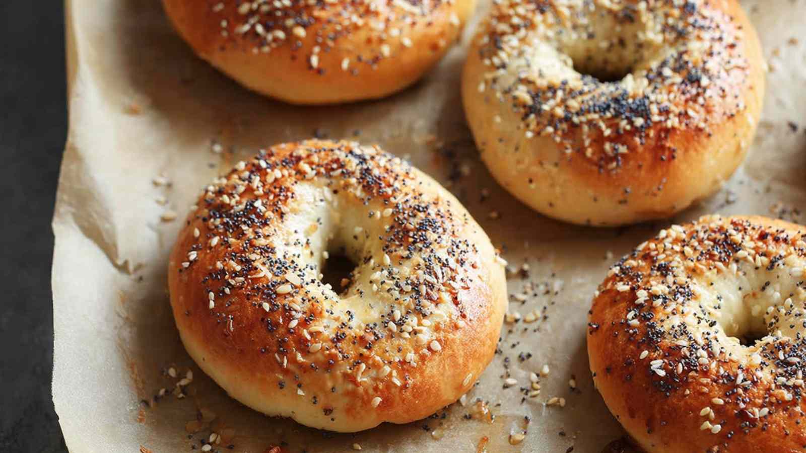 Up-close shot of golden-brown gluten free bagels topped with sesame, poppy seeds, and seasoning on parchment paper