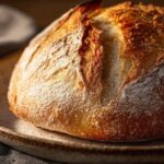Golden brown sourdough bread with a crackly crust made using bolted flour, resting on a rustic ceramic plate