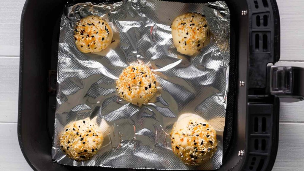 Hands shaping dough balls and stuffing each with a cube of cream cheese for the bagel minis