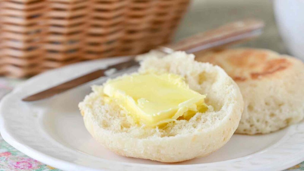 An English muffin sliced open with a pat of butter melting on the fluffy, textured inside