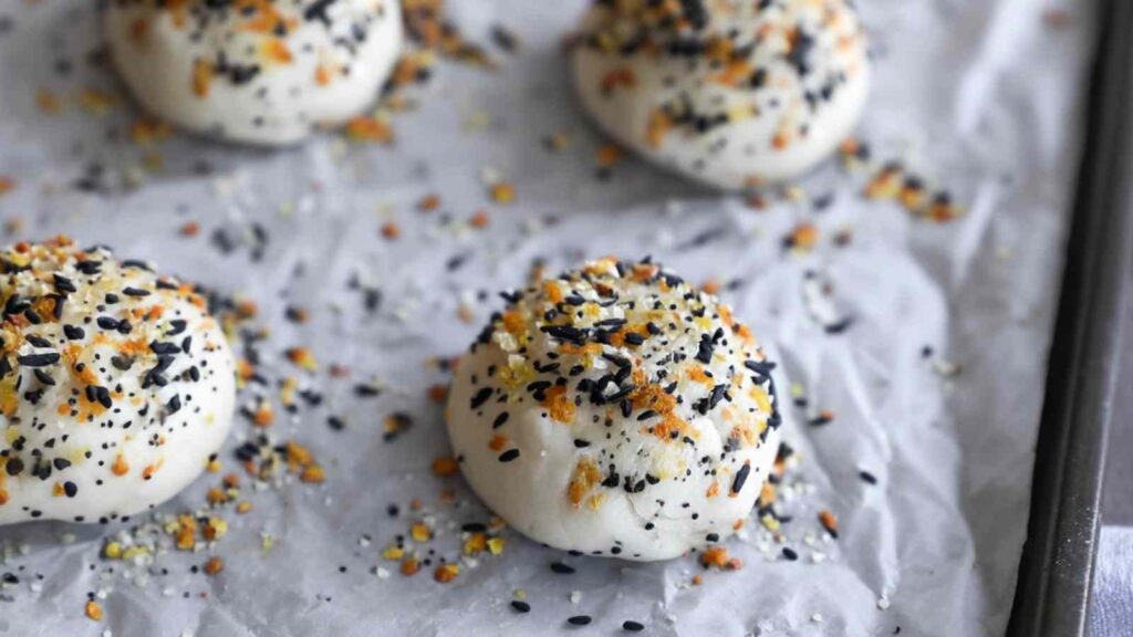 Shaped dough balls topped with everything seasoning blend, resting on parchment before baking