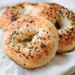 Three low carb bagels resting on a cloth, sprinkled with sesame and black seeds, showing a crisp, golden crust