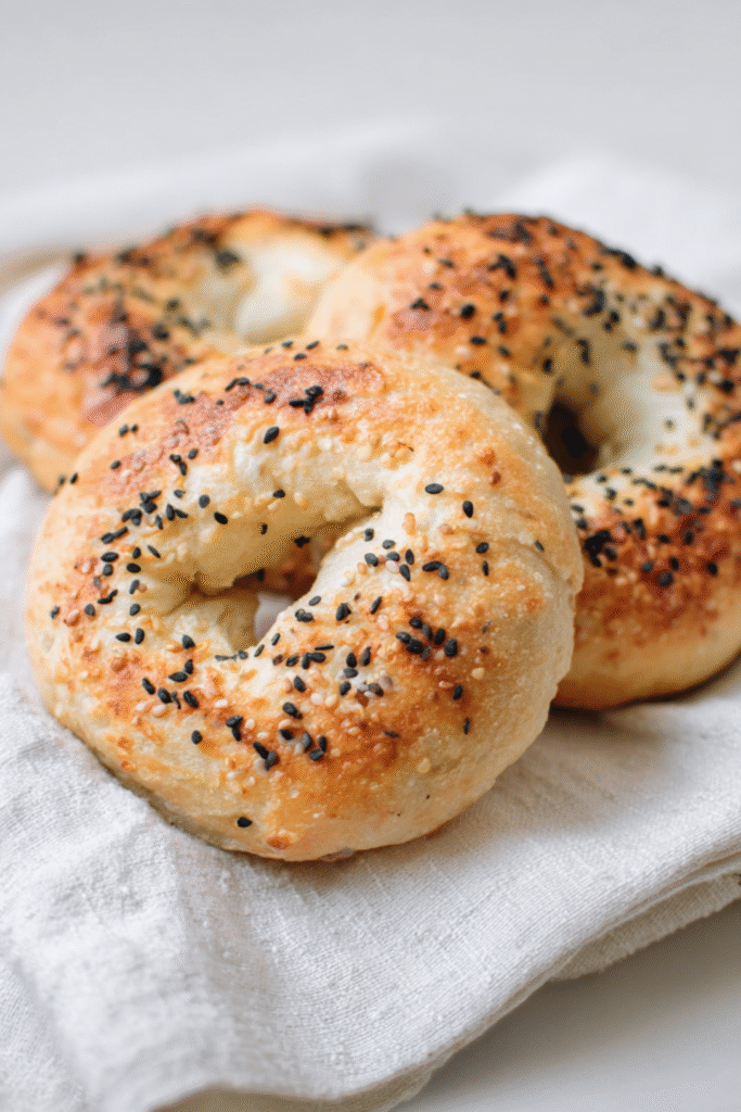 Three low carb bagels resting on a cloth, sprinkled with sesame and black seeds, showing a crisp, golden crust