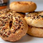 Stack of Thomas' high protein bagels topped with everything seasoning on a white plate, showcasing their golden crust and chewy texture