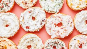 Overhead view of open bagels topped with a variety of cream cheese spreads on a coral background.