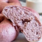 Close-up of a sliced strawberry bagel showing its airy, fluffy interior with a vibrant natural pink hue, set against whole pink bagels.