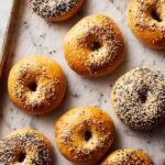 Top-down view of freshly baked bagels with sesame and poppy seeds on baking tray