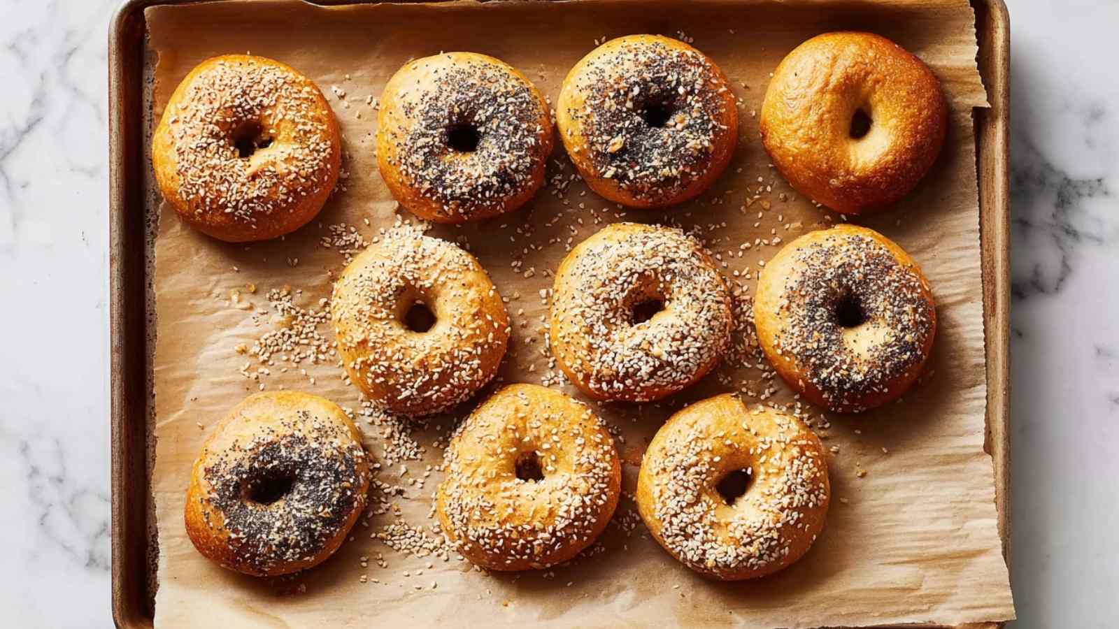 Top-down view of fresh baked bagels on parchment paper with scattered seeds