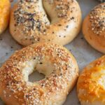 Freshly baked bagels topped with sesame, poppy seeds, and cheese, ready to be served with whipped cream cheese