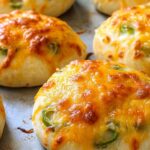 Close-up of freshly baked green chile bagels with bubbling cheddar cheese on a baking tray