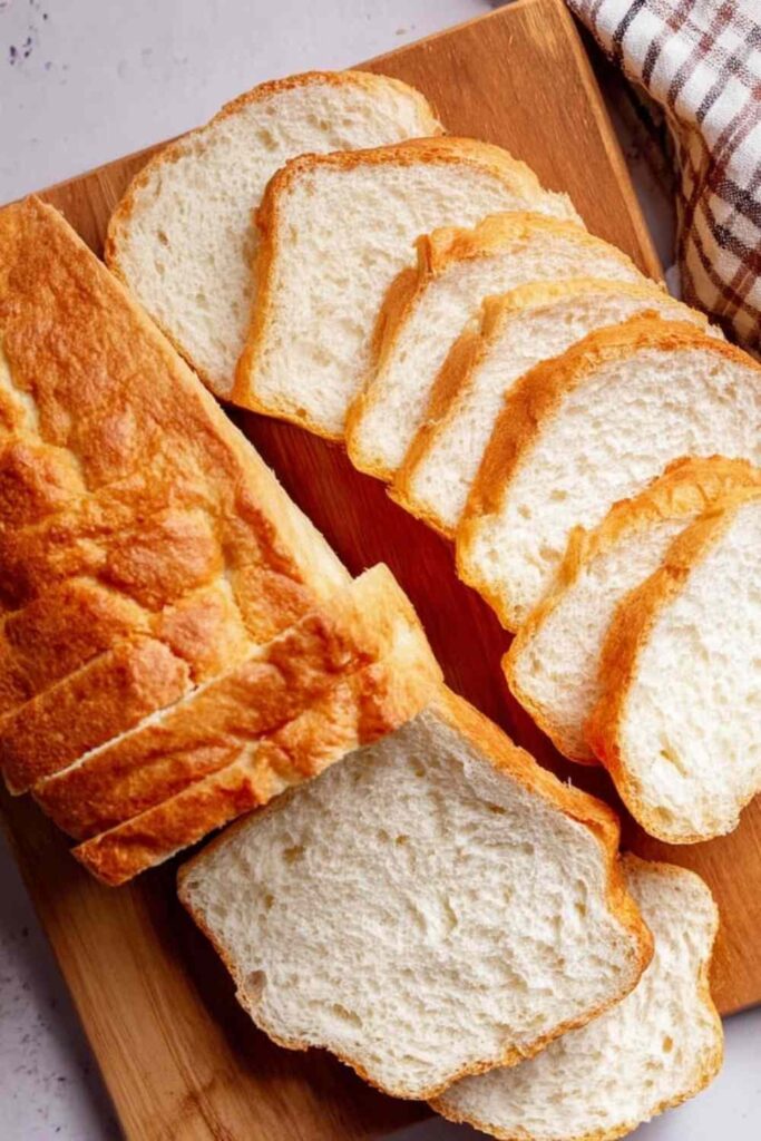 Overhead view of a golden loaf of sliced protein bread on wooden board with light crust and soft crumb