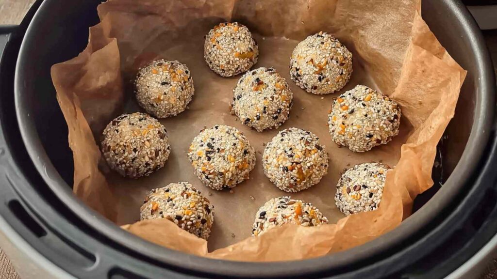 Keto everything bagel bites arranged in parchment-lined air fryer basket before cooking
