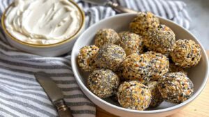 A bowl of golden air fryer bagel bites coated in everything seasoning, served with whipped cream cheese on a striped towel