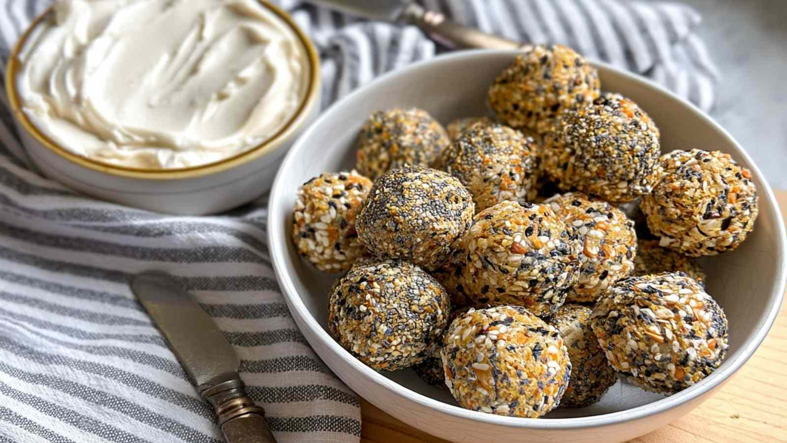 A bowl of golden air fryer bagel bites coated in everything seasoning, served with whipped cream cheese on a striped towel