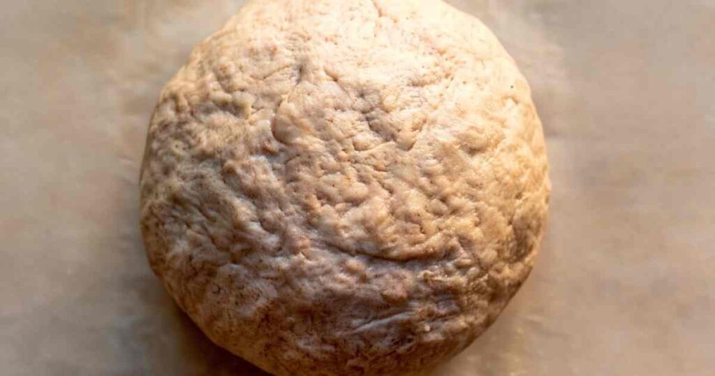 Smooth ball of high protein bagel dough on parchment paper, showing elastic texture