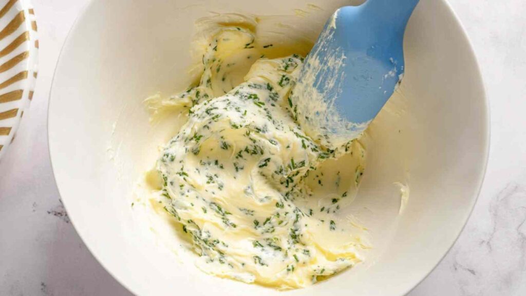 Cream cheese mixed with chopped herbs in a bowl using a spatula, mid-preparation