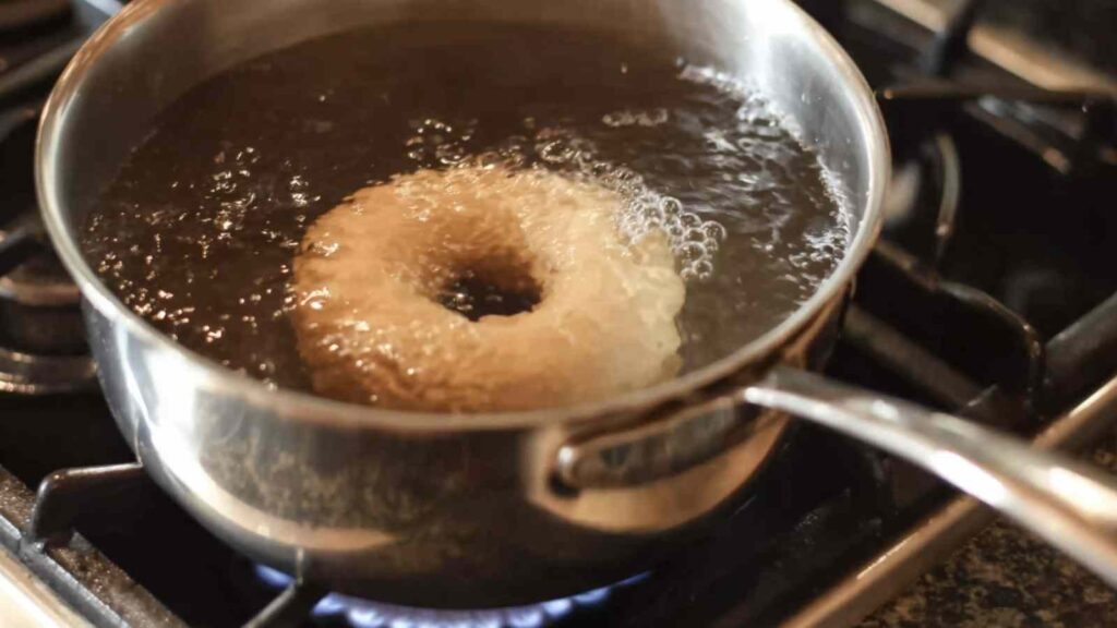 Gluten free bagel being boiled in molasses water in a stainless pot to prep for baking