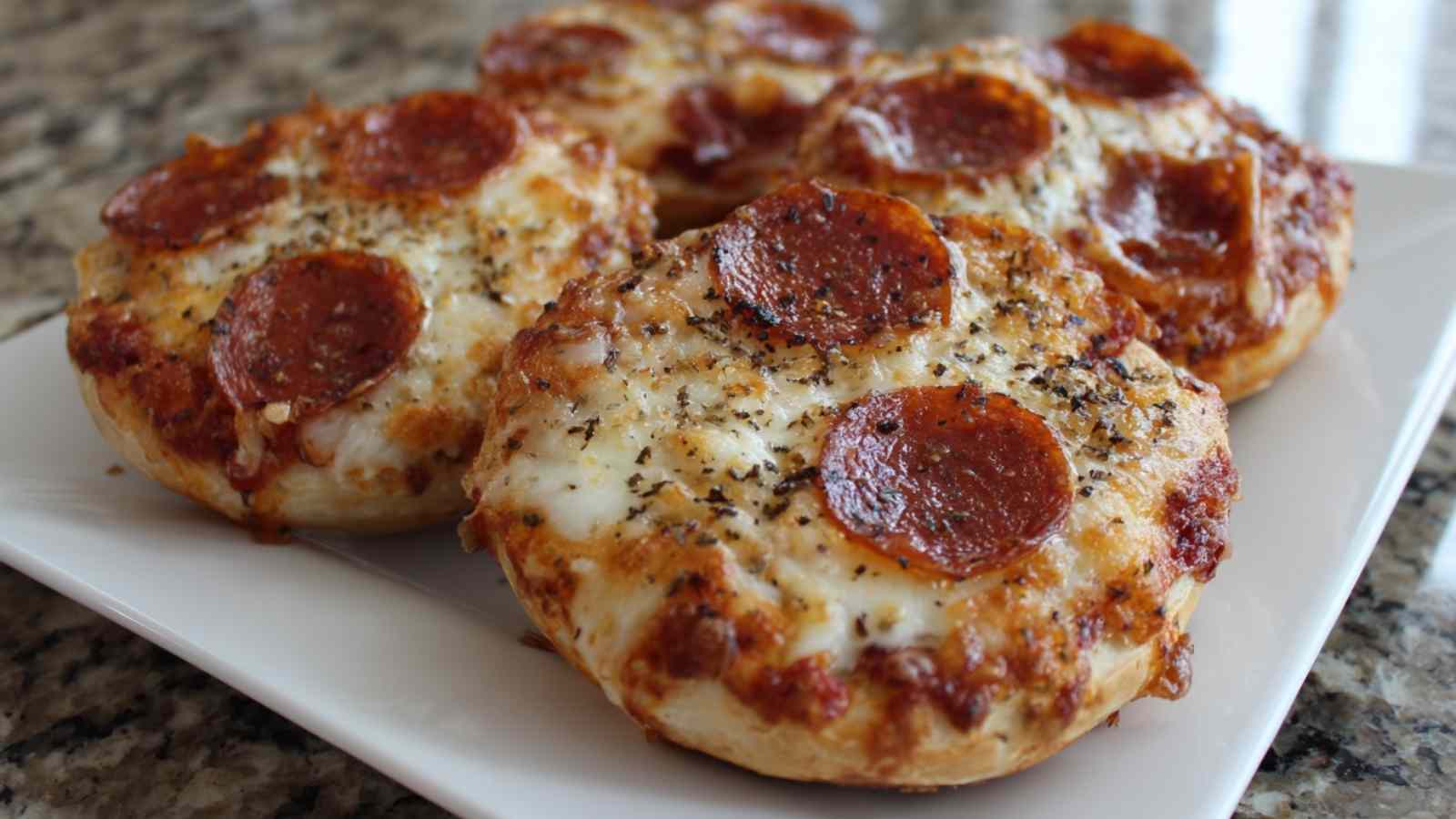 Close-up of golden-brown air fryer bagel bites with melted mozzarella and crispy pepperoni slices on a white plate.