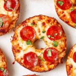 Close-up of crispy pizza bagels topped with melted mozzarella, pepperoni, and fresh basil, cooked in an air fryer.