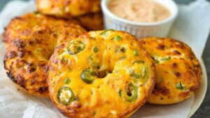 Close-up of golden jalapeño cheddar bagels with melted cheese and sliced jalapeños, with Greek yogurt salsa dip in the background