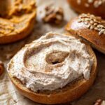 Pumpkin bagel spread with thick pecan cinnamon cream cheese, surrounded by pecans and rustic textures.