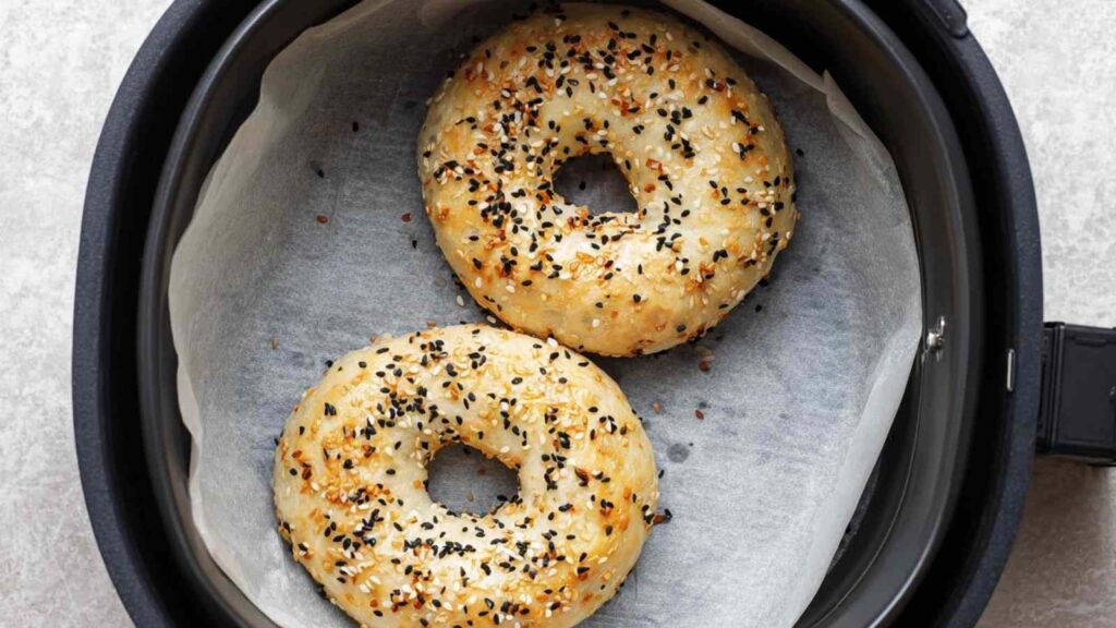 Uncooked air fryer bagels placed on parchment inside an air fryer basket