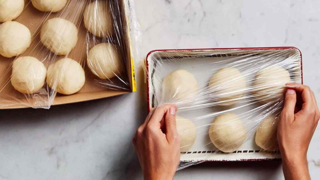 Two trays of dough balls covered with plastic wrap