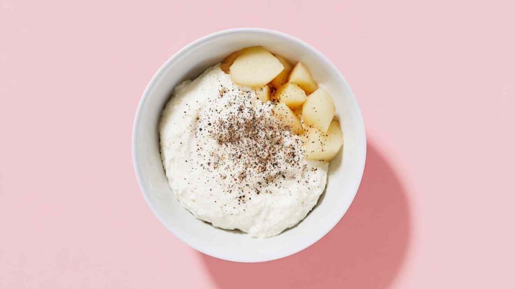 Cream cheese in a bowl with roasted garlic cloves and cracked black pepper.