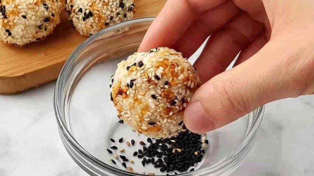 A hand dipping a dough ball in a bowl of everything bagel seasoning
