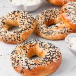 Golden sesame bagels topped with seeds, served with a bowl of whipped cream cheese on a white surface