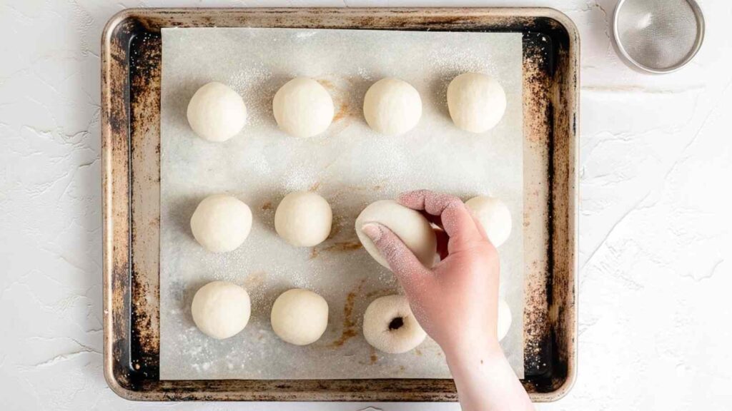 Hand shaping mini bagel dough balls on a parchment-lined baking sheet before poking holes in th
