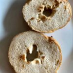 Two plain, sliced bagel halves resting on a white plate, ready for toasting