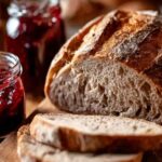 Sliced bolted flour sourdough bread on a wooden board with jars of red jam beside it