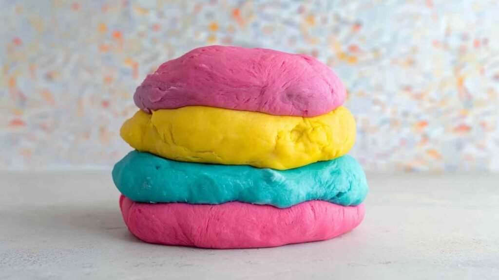 Stack of brightly colored dough layers—pink, yellow, blue—used for making rainbow bagels.