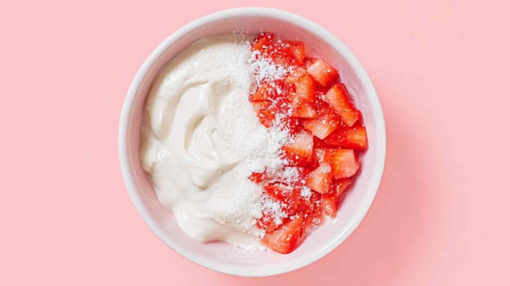 Bowl with whipped cream cheese, diced strawberries, and powdered sugar on pink background.