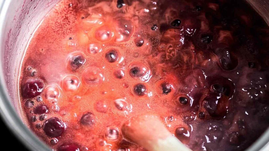 Bubbling pot of strawberry filling with visible fruit pieces, releasing aroma and color for bagel dough.