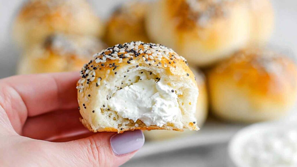 Hand holding a stuffed everything bagel bite with a bite taken out, showing the cream cheese filling