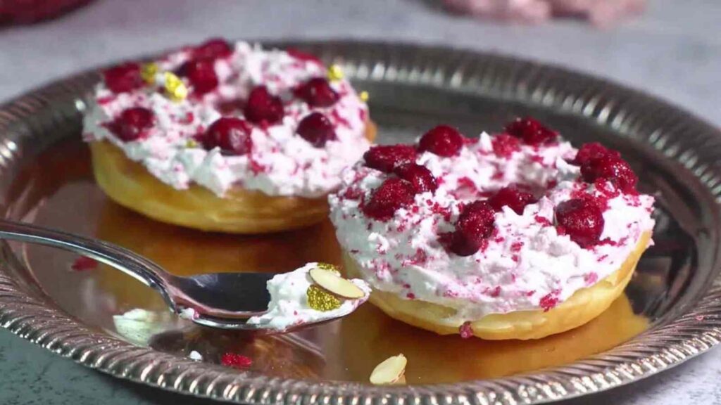 Two cottage cheese bagels topped with whipped cream and red berries, served on a silver tray with a spoon.