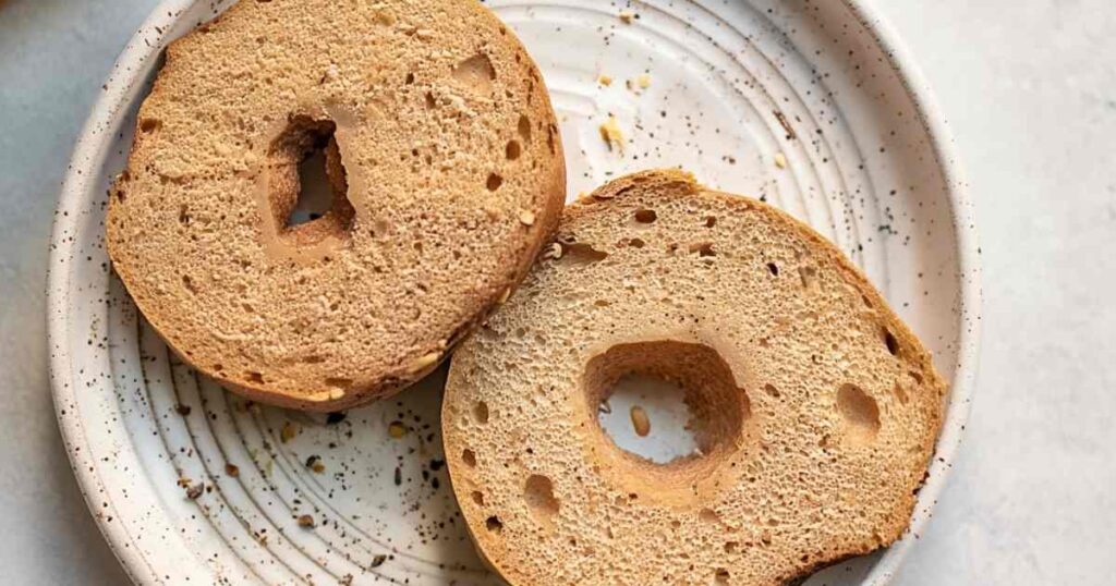 Sliced open Thomas' high protein bagel on speckled plate showing dense, uniform crumb texture