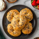Top-down view of cottage cheese bagels on a dark plate with seasoning, cream, and fresh strawberries on the side.