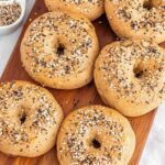 Whole wheat bagels simmering in a pan of water on the stovetop, steam rising