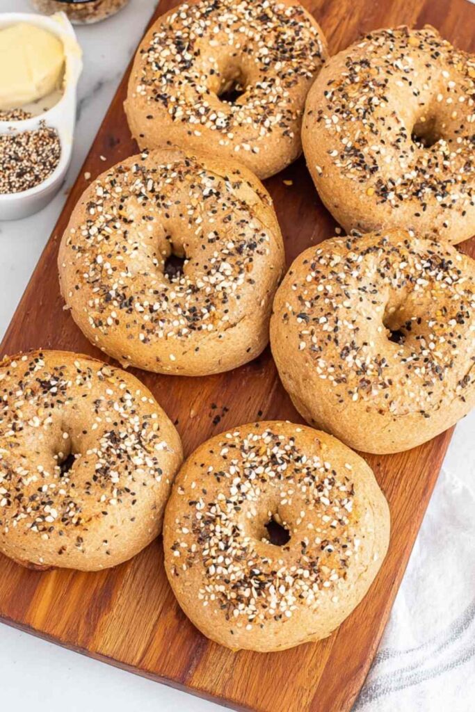 Whole wheat bagels simmering in a pan of water on the stovetop, steam rising