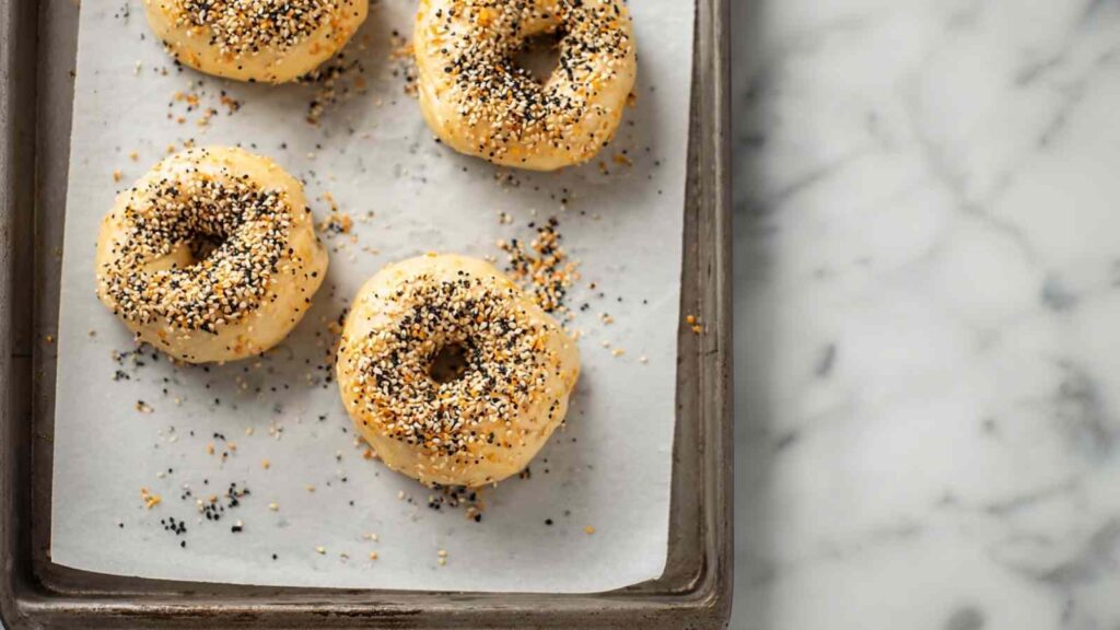 Raw cottage cheese bagels on a parchment-lined baking tray topped with everything seasoning.
