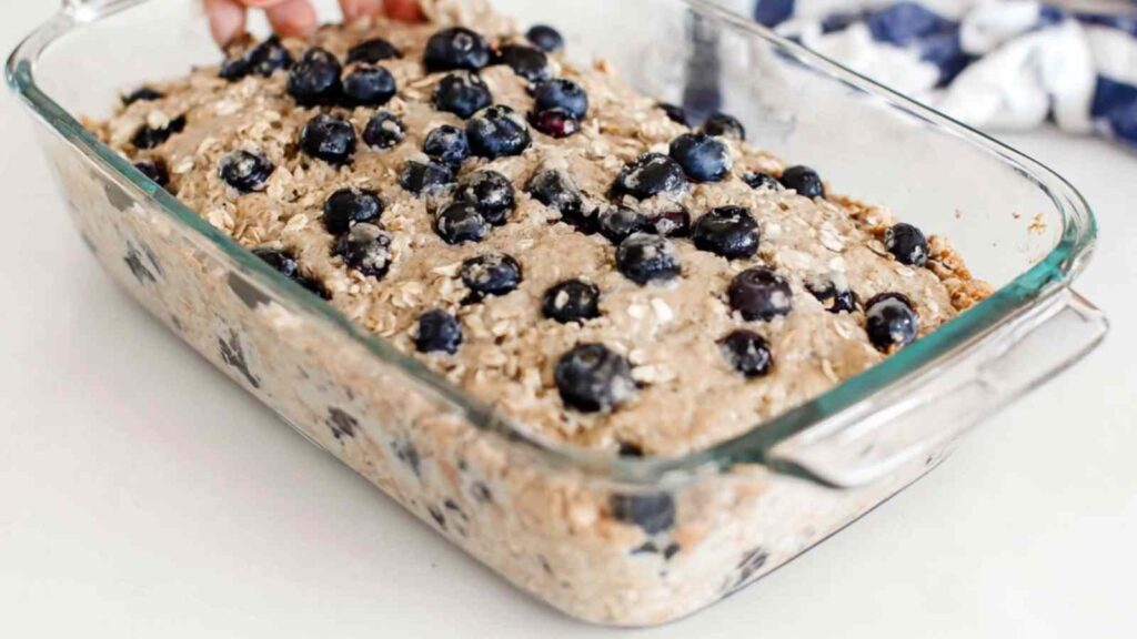 Unbaked blueberry oat bread batter in a clear glass loaf pan topped with fresh blueberries