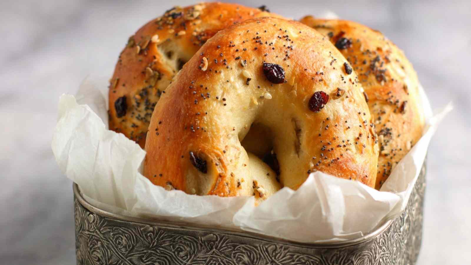Golden brown vegan bagels with sun dried tomatoes and basil in a parchment-lined decorative tin