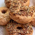 Vertical stack of everything-seasoned Thomas' high protein bagels on white surface, close-up showing texture